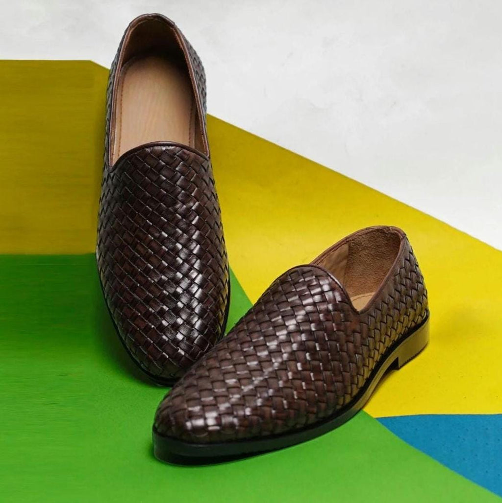 Men's woven leather loafers in dark brown, worn with black pants, featuring a sleek slip-on style and textured finish for formal or casual wear.